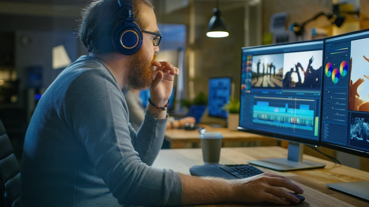 Editor working on a multi-clip timeline and colour grading panels across dual monitors in a studio