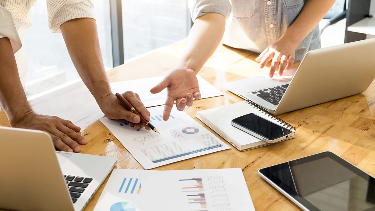 Two people reviewing printed performance charts and a sales report across a shared desk