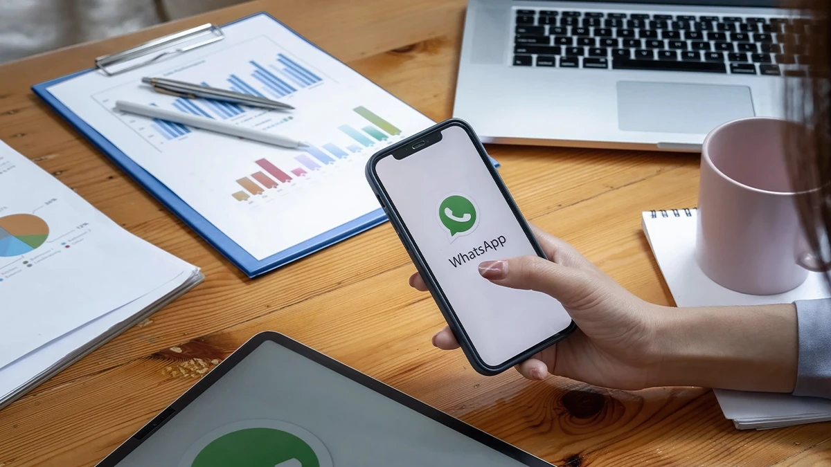 Hand holding a phone with a messaging app open beside printed performance charts and a laptop
